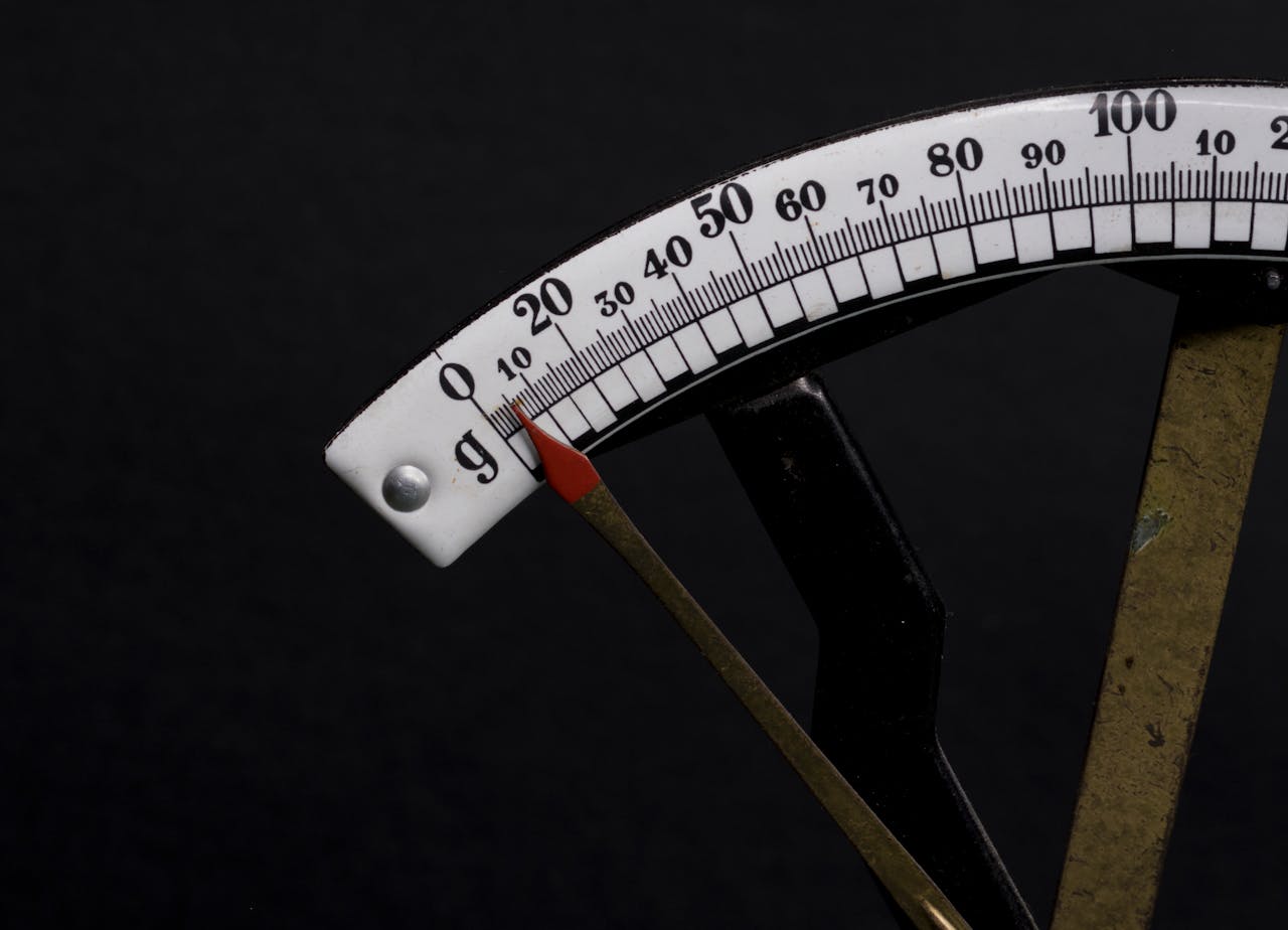 Detailed close-up image of a vintage analog weighing scale with a pointer against a black background.