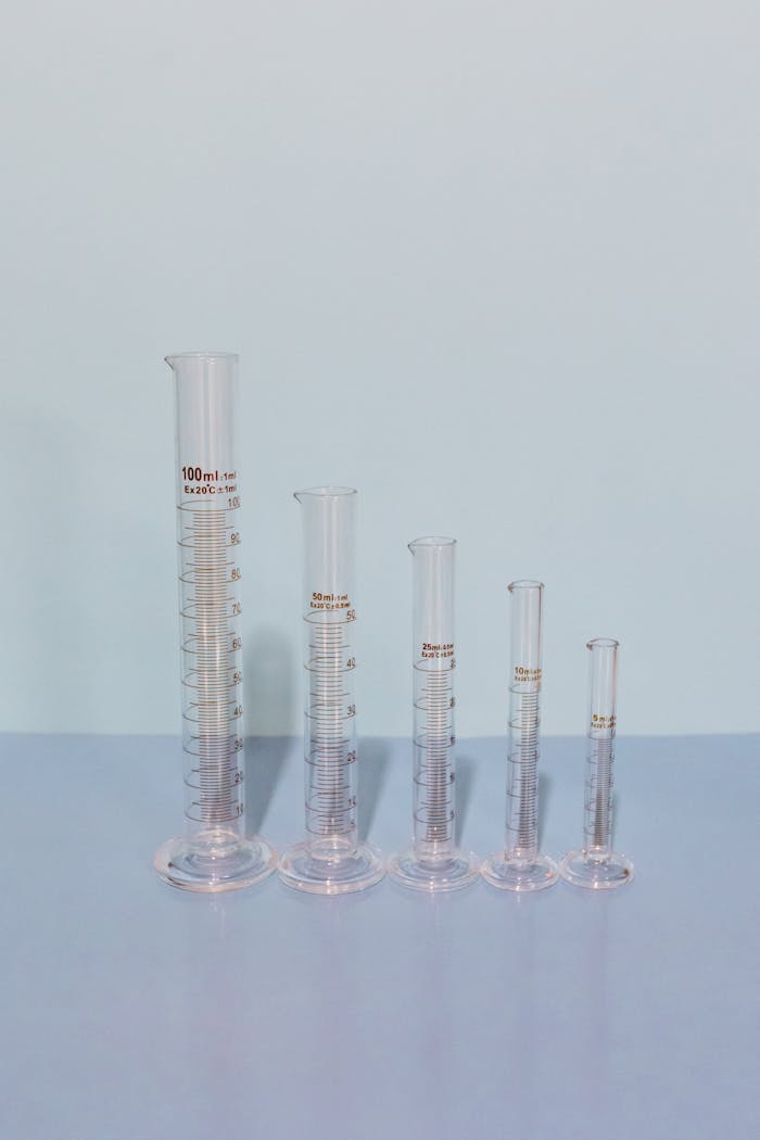 Vertical shot of empty glass graduated cylinders in various sizes, ideal for laboratory use.